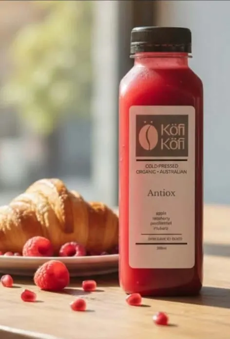 A bottle of Köfi Köfi Antiox cold-pressed juice with a croissant and fresh raspberries