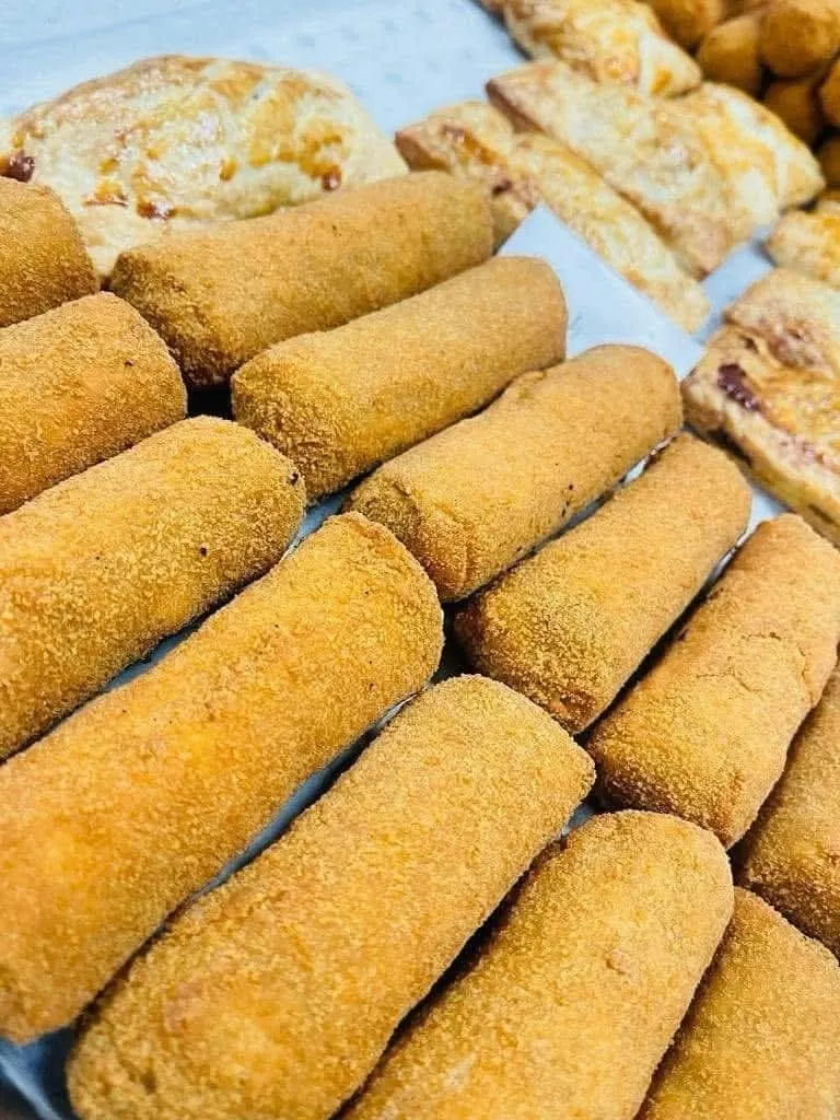 A tray of golden crumbed croquettes beside baked pastries