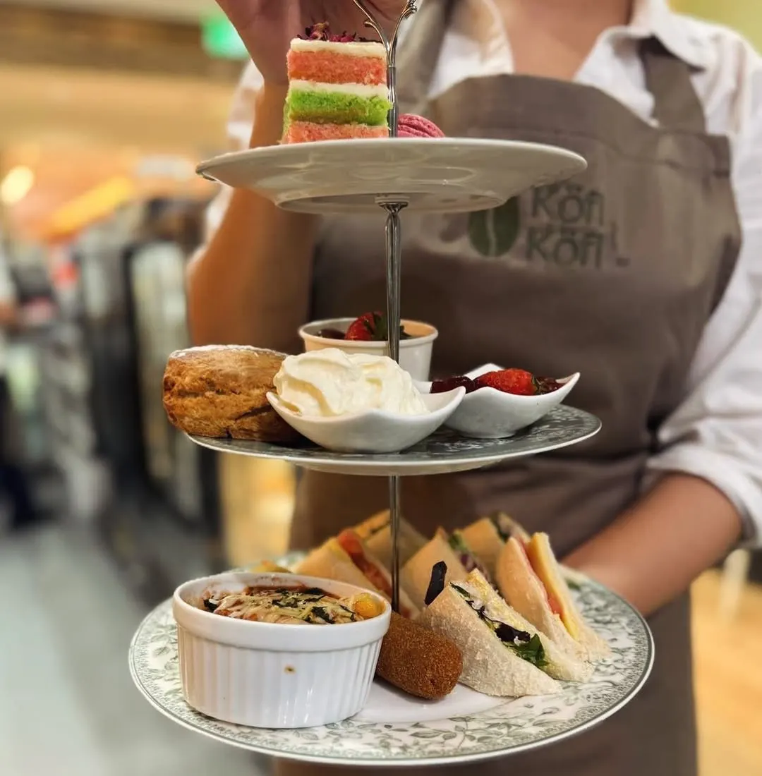 Scones with jam and cream beside a layered ribbon cake on a high tea stand