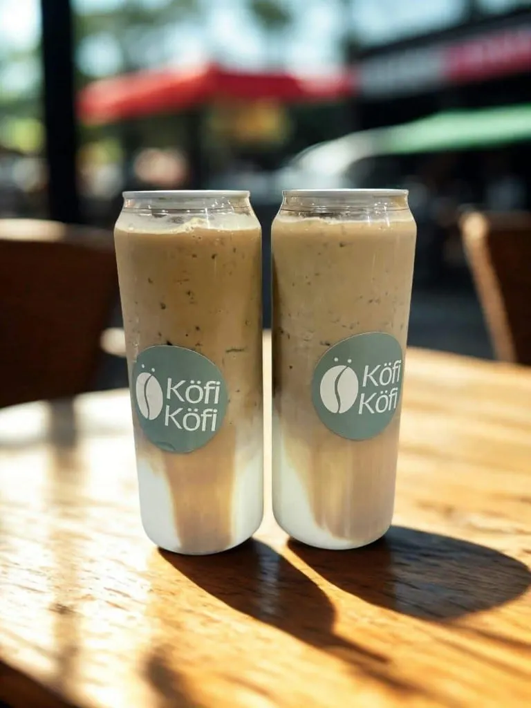 Two iced lattes in Köfi Köfi cans on a cafe table
