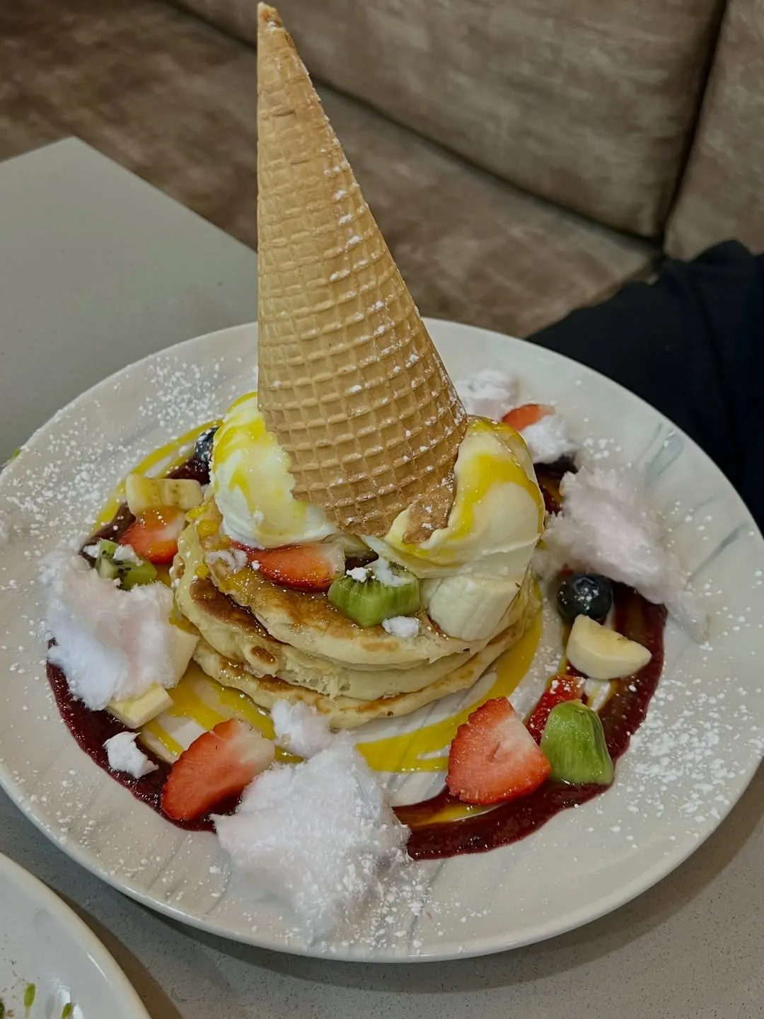 Pancakes topped with fresh strawberries, banana, coconut and a waffle cone