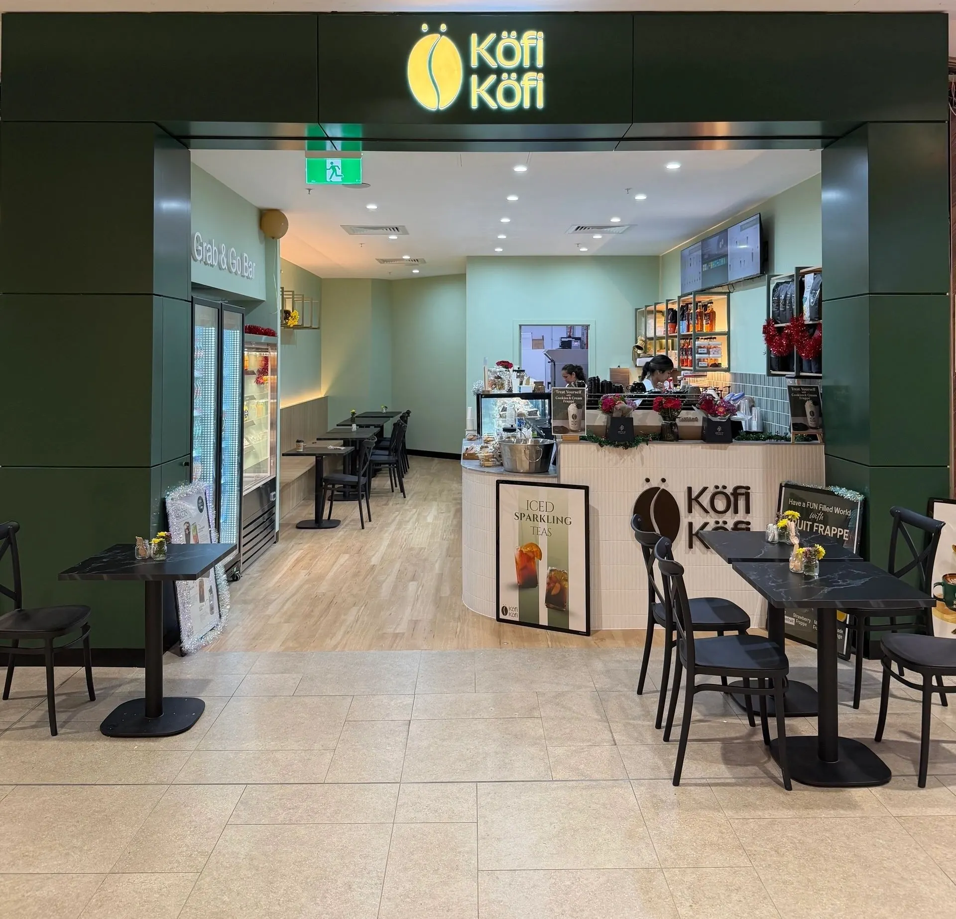 The Köfi Köfi cafe at HomeCo Brandon Park: green shopfront with the lit Köfi Köfi sign, the Grab & Go bar, the counter and tables out front